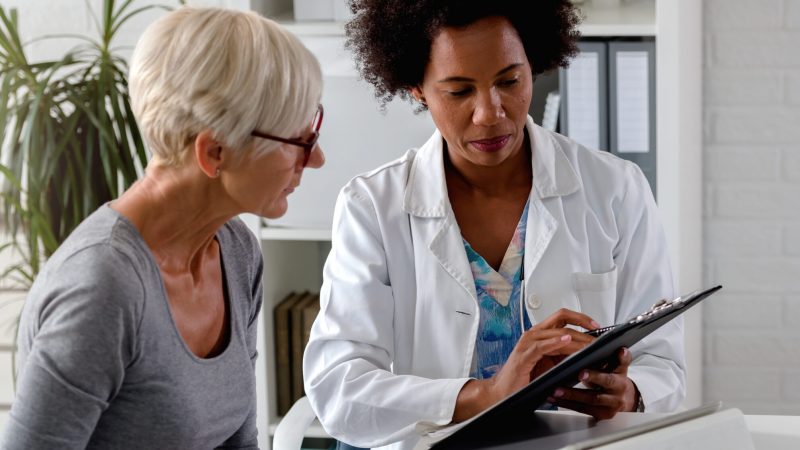 A female doctor sits at her desk and chats to an elderly female patient while looking at her  test results